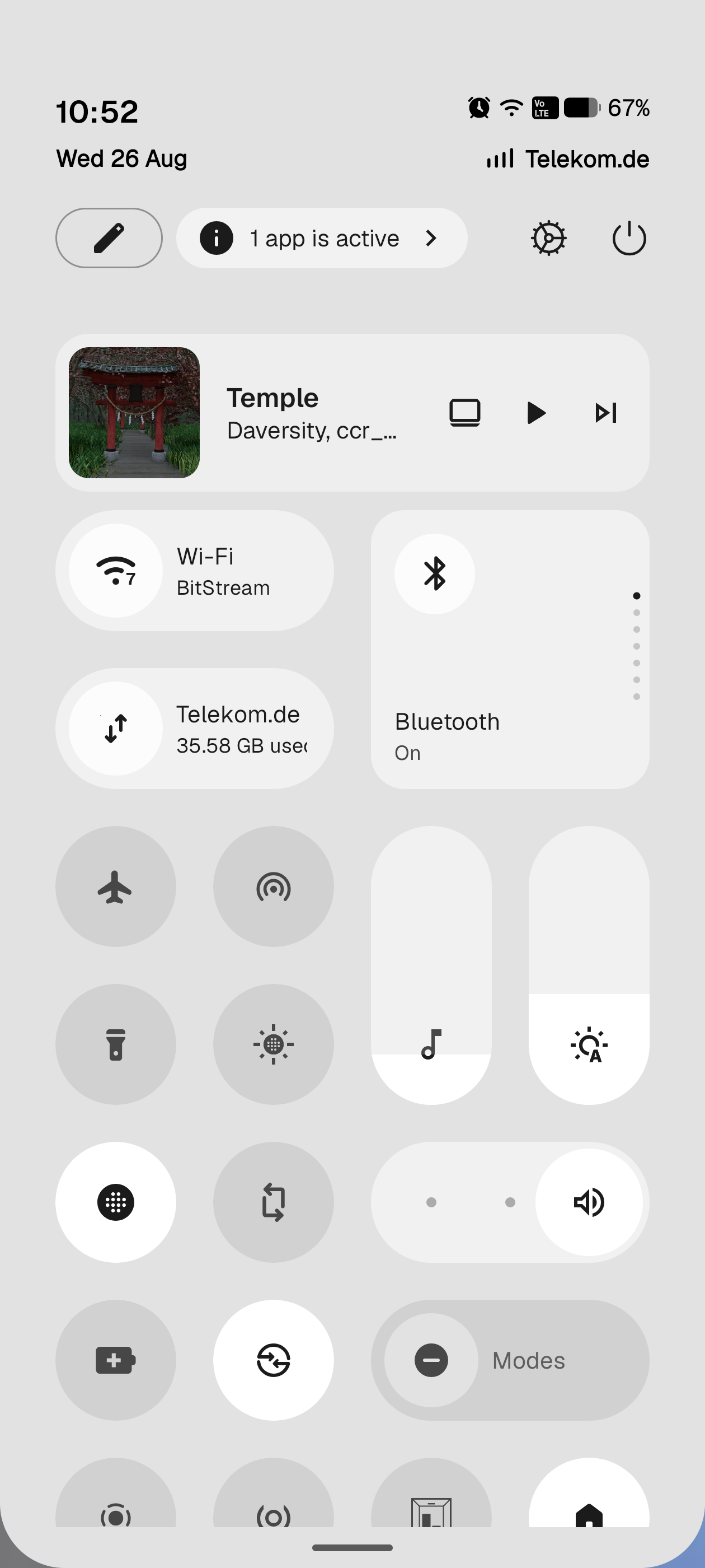 The separate Quick Settings panel: an app is active privacy chip at the top, a media player, wide Wi-Fi, mobile data and Bluetooth tiles, then round toggles and vertical brightness and volume sliders.